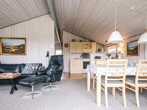A modern living room with a black leather sofa, a dining table with chairs, and a kitchen area with wooden cabinets and a microwave. - 6 Person Holiday Home in Hemmet (Hemmet)