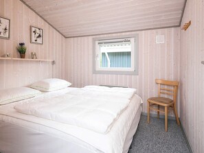 Quarto com cama, uma cadeira, janela e prateleira com objetos decorativos.