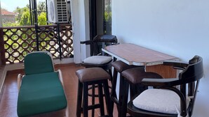 Un balcon avec une table et des chaises, un fauteuil vert rembourré et un appareil de climatisation.