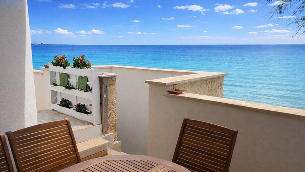 A balcony with a wooden table and chairs, overlooking a clear blue sea. - Seafront Apartment, ideal for Families (Torre Lapillo)