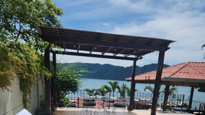 Un espace aménagé au bord de la piscine, avec des chaises longues et une pergola offrant une vue sur un plan d’eau.