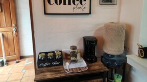 Un coin café aménagé avec des bocaux, une machine à café et un panneau indiquant : « Café, s’il vous plaît ».