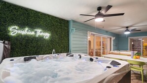 A hot tub with a neon sign reading "Sunshine Therapy" against a green wall, a ceiling fan, and a table with chairs outside. - Sleeps 20! Pickleball, Heated Pool, Hot Tub & Games Retreat! Near Beaches (Bradenton)