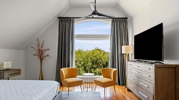 Une chambre à coucher comprenant un lit, deux fauteuils, une petite table, un téléviseur et une commode.