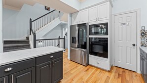 Une cuisine moderne avec des meubles blancs, des appareils en acier inoxydable et un escalier en bois.