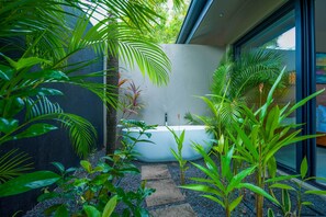 A modern bathroom with a freestanding bathtub, surrounded by lush greenery and a stone pathway. - Premium Location Gated Beach Community Villa (Tamarindo)