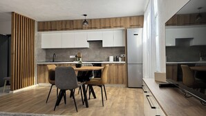 A modern kitchen with wooden accents, a dining area with a wooden table and chairs, and a large window providing natural light. - Central Apartment (Zetea)