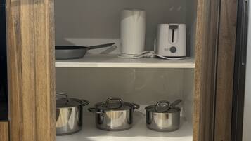 Un pensile da cucina con tre pentole in acciaio inossidabile sullo scaffale inferiore e una bollitore elettrico bianco e una padella sullo scaffale superiore.