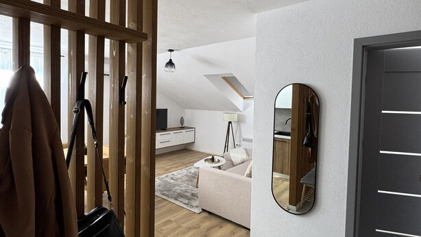 A modern living room with a wooden partition, a grey sofa, a round mirror, and a grey bench. - Central Apartment (Zetea)