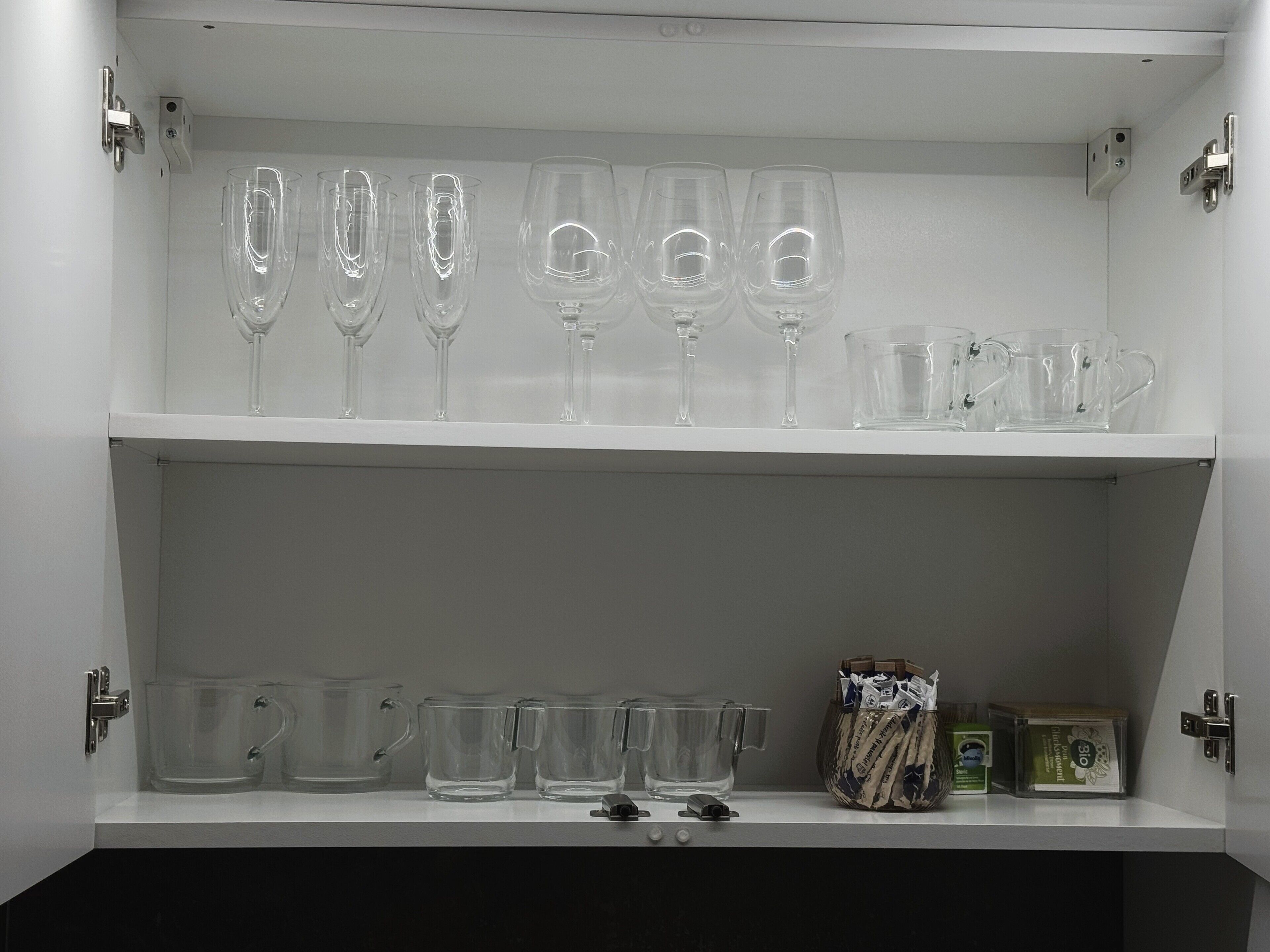 Ein Schrank mit Regalen, auf denen verschiedene Gläser, darunter Weinkelche und Tumbler, stehen.