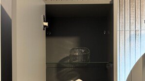 A storage cabinet with multiple shelves, a glass container, and a tissue box. - Central Apartment (Zetea)
