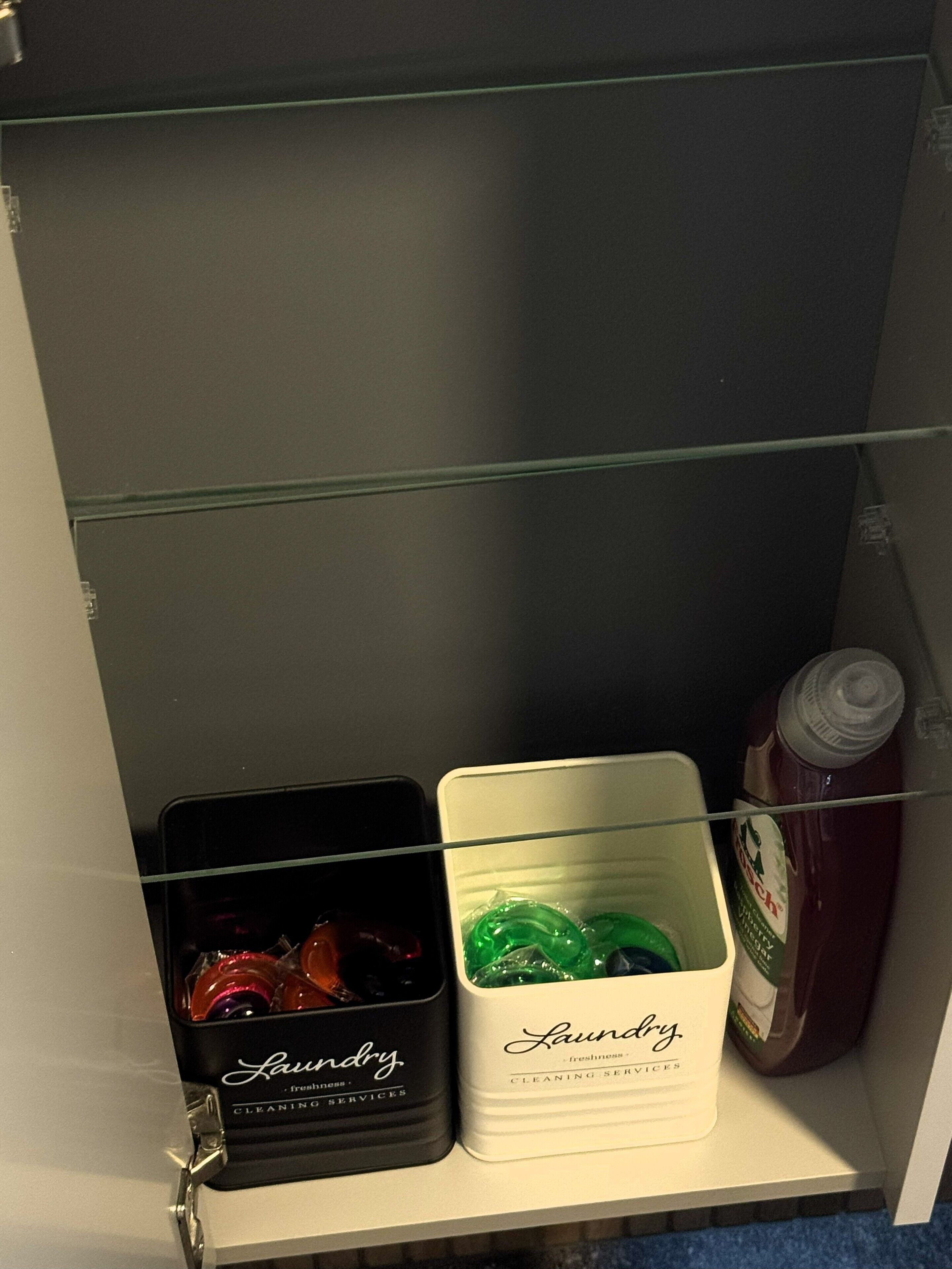 Ein Stauraum mit zwei beschrifteten Behältern, einer für Wäsche und einer für Reinigungsservice, sowie eine Ketchupflasche.