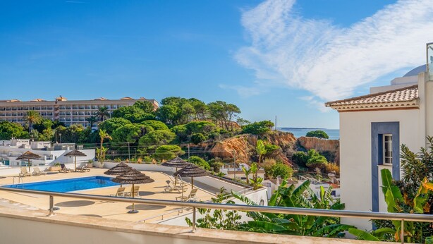 A rooftop pool area with lounge chairs and umbrellas, overlooking a coastal landscape with buildings and trees. - T2 Luminoso c/Piscina perto da Praia by LovelyStay (Olhos de Água)