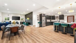 Une cuisine moderne avec des meubles de couleur sombre, un réfrigérateur en acier inoxydable et un coin bar agrémenté de tabourets verts.