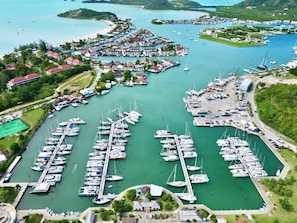 An aerial view of a marina with numerous boats docked, surrounded by lush greenery and residential buildings. - Luxury waterfront villa jolly harbour Antigua (Jolly harbour)