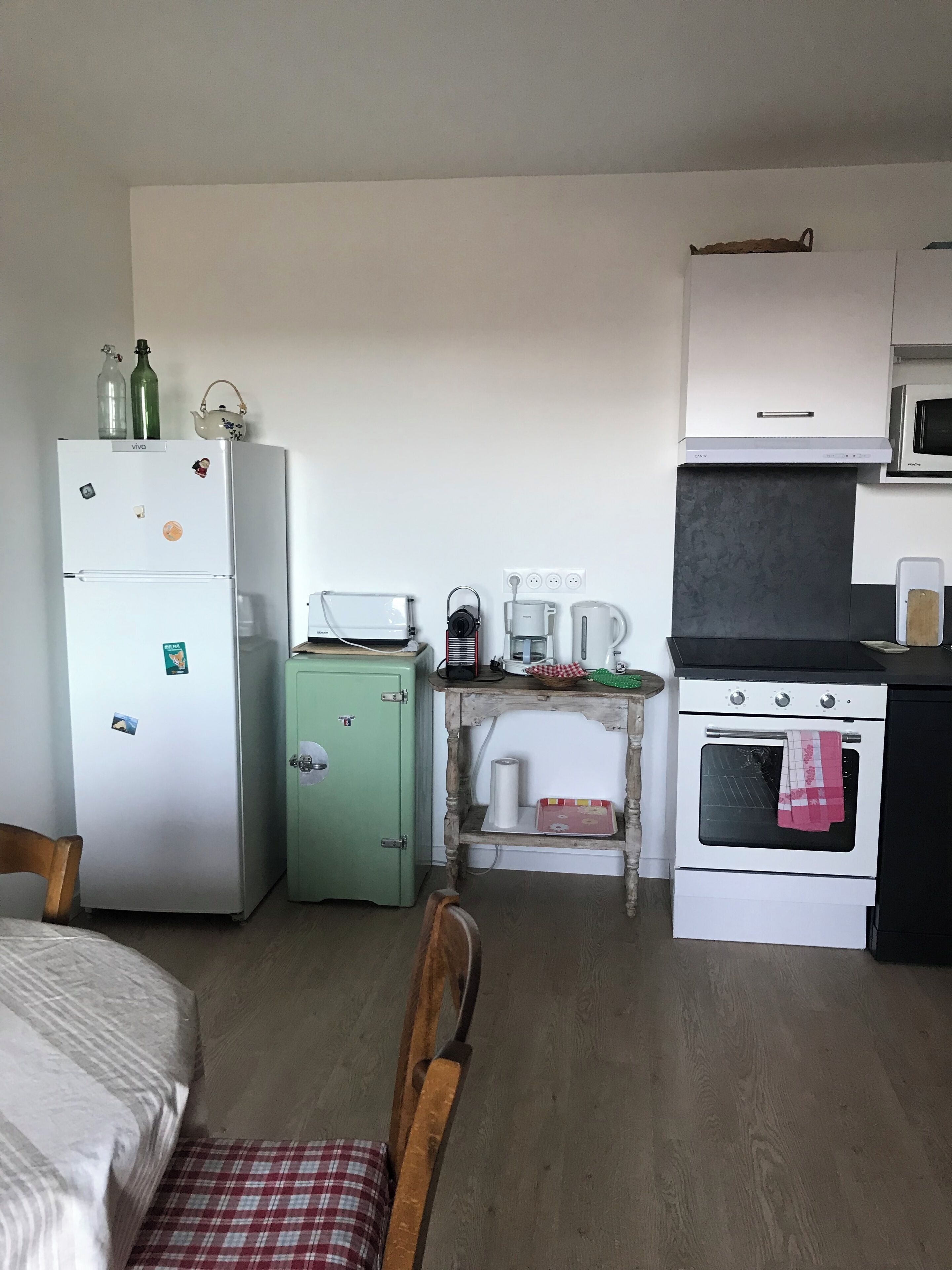 Una cocina compacta equipada con refrigerador, microondas, estufa y una pequeña mesa con tetera y hervidor.