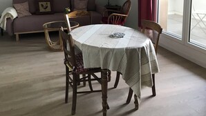 A dining area with a round table, chairs, a hanging light fixture, a sofa, and a window with curtains. - Cosy nest in pont l'évêque (pont l eveque)