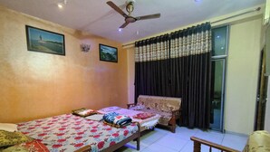 A bedroom with a bed, a chair, a ceiling fan, and a window with curtains. - MAHAKALI HOMESTAY (Garudeshwar)