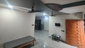 A room with a bench, ceiling fans, a tiled floor, and a wooden door. - MAHAKALI HOMESTAY (Garudeshwar)