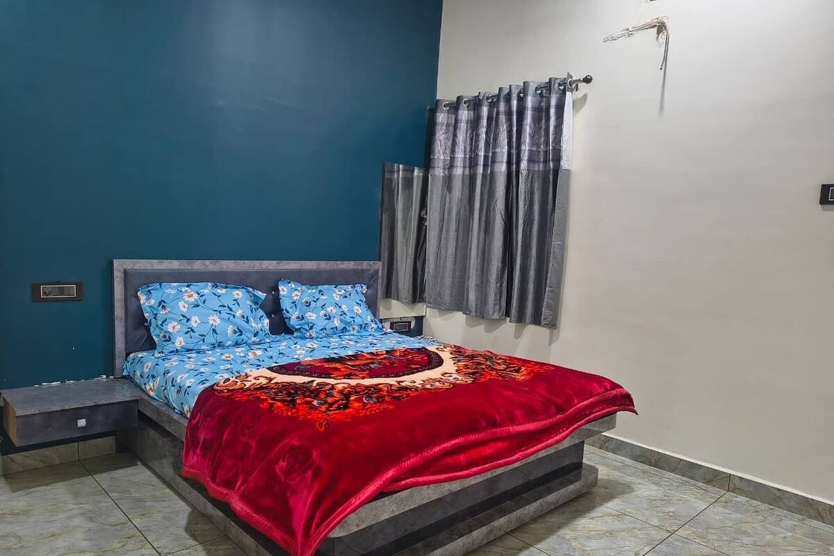 A bedroom with a bed, nightstands, a red blanket, and a window with curtains.
