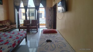 A room with a bed, a sofa, a TV mounted on the wall, and a ceiling fan. - MAHAKALI HOMESTAY (Garudeshwar)