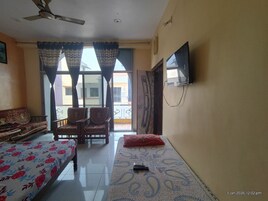 A room with a bed, a sofa, a TV mounted on the wall, and a ceiling fan.