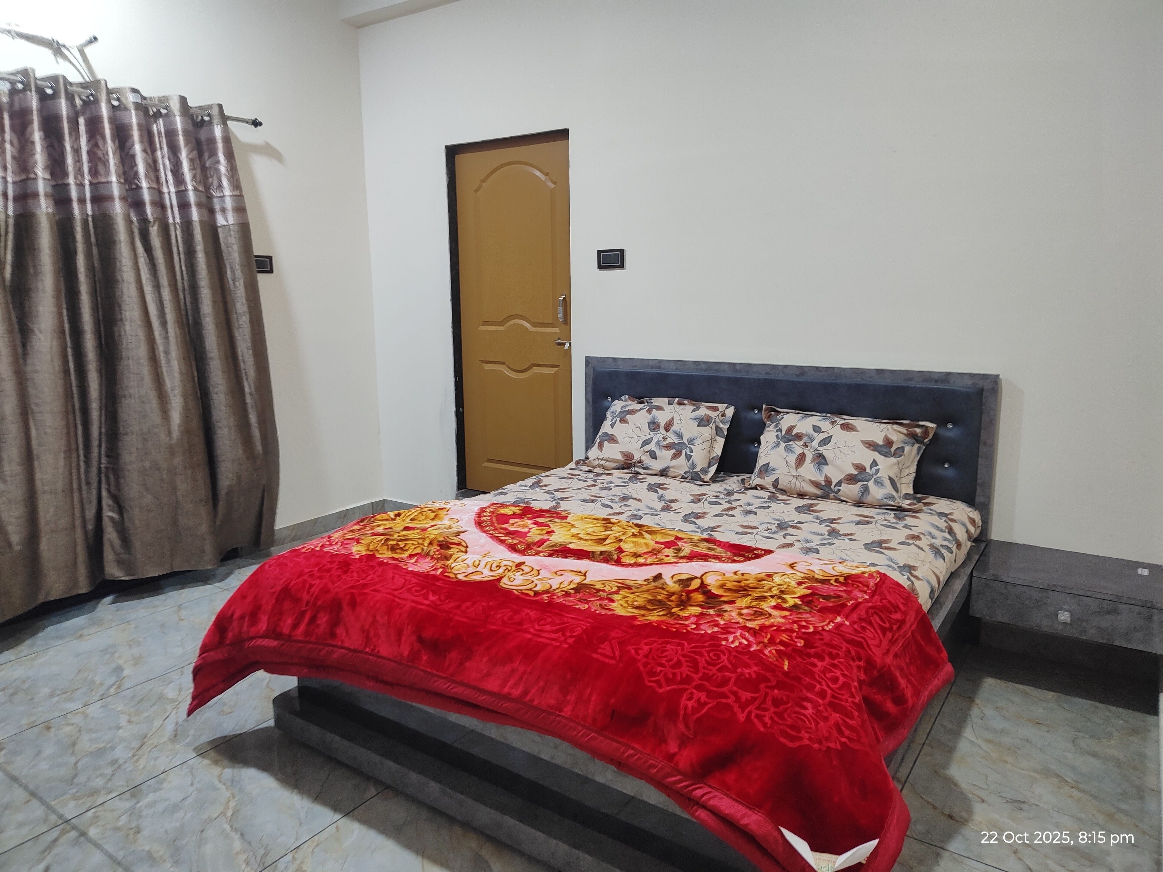 Un dormitorio con cama, cortinas, una puerta y una mesita de noche.