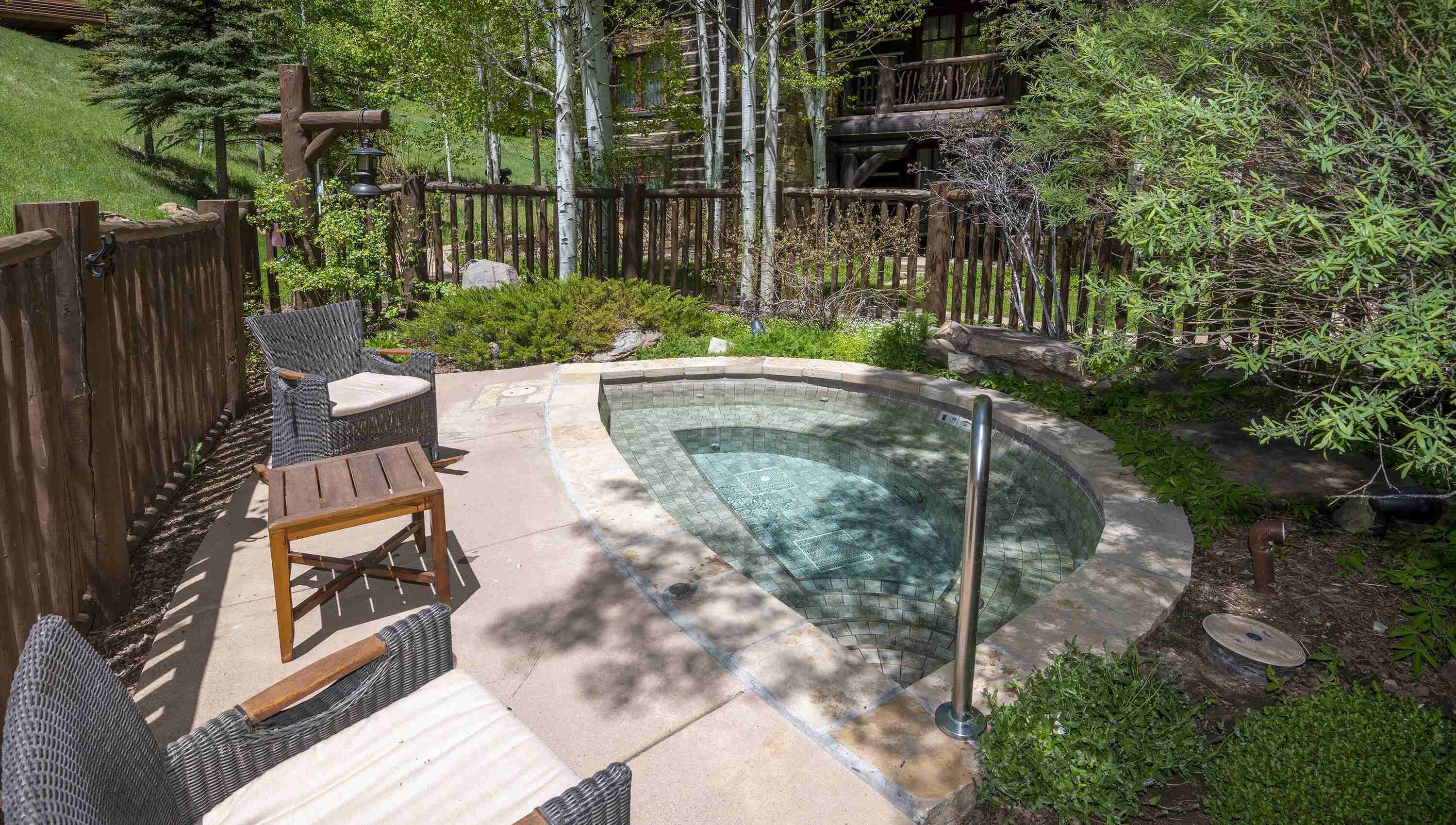 A backyard with a swimming pool, wooden deck, wicker furniture, and a wooden fence.