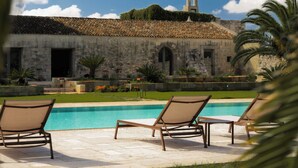 A pool area with lounge chairs and a stone building with a tiled roof in the background. - Masseria Eirene (Lecce)