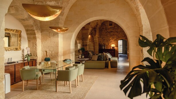 A spacious living area with a glass dining table, green chairs, and a stone archway. - Masseria Eirene (Lecce)