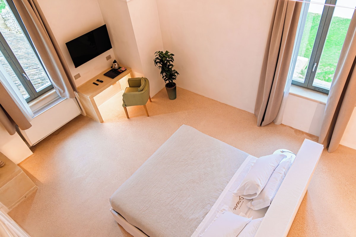 A hotel room with a bed, a desk with a chair, a television, and a potted plant.