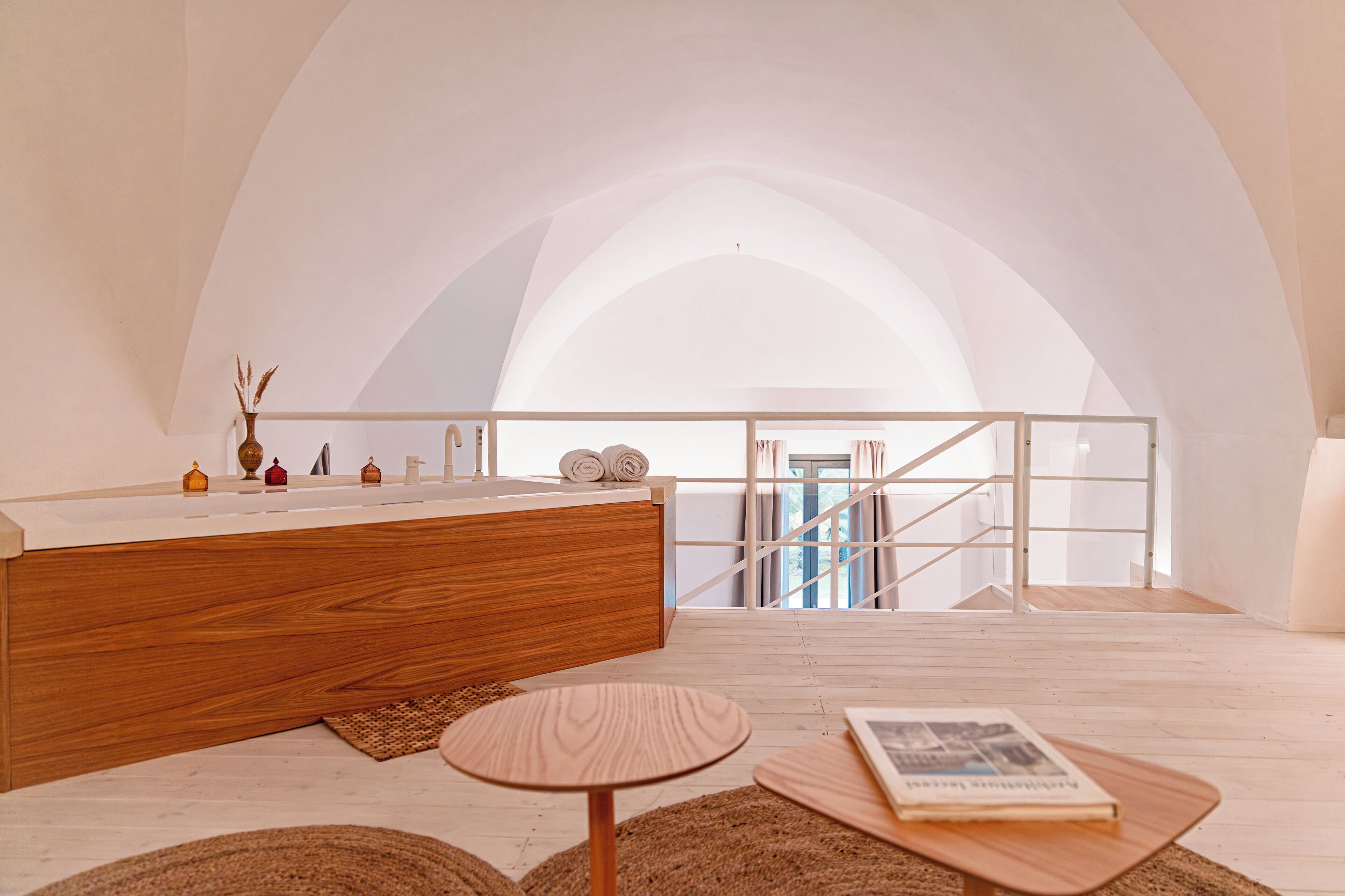 A modern bathroom with a wooden vanity, a round wooden table, and a view of a staircase.