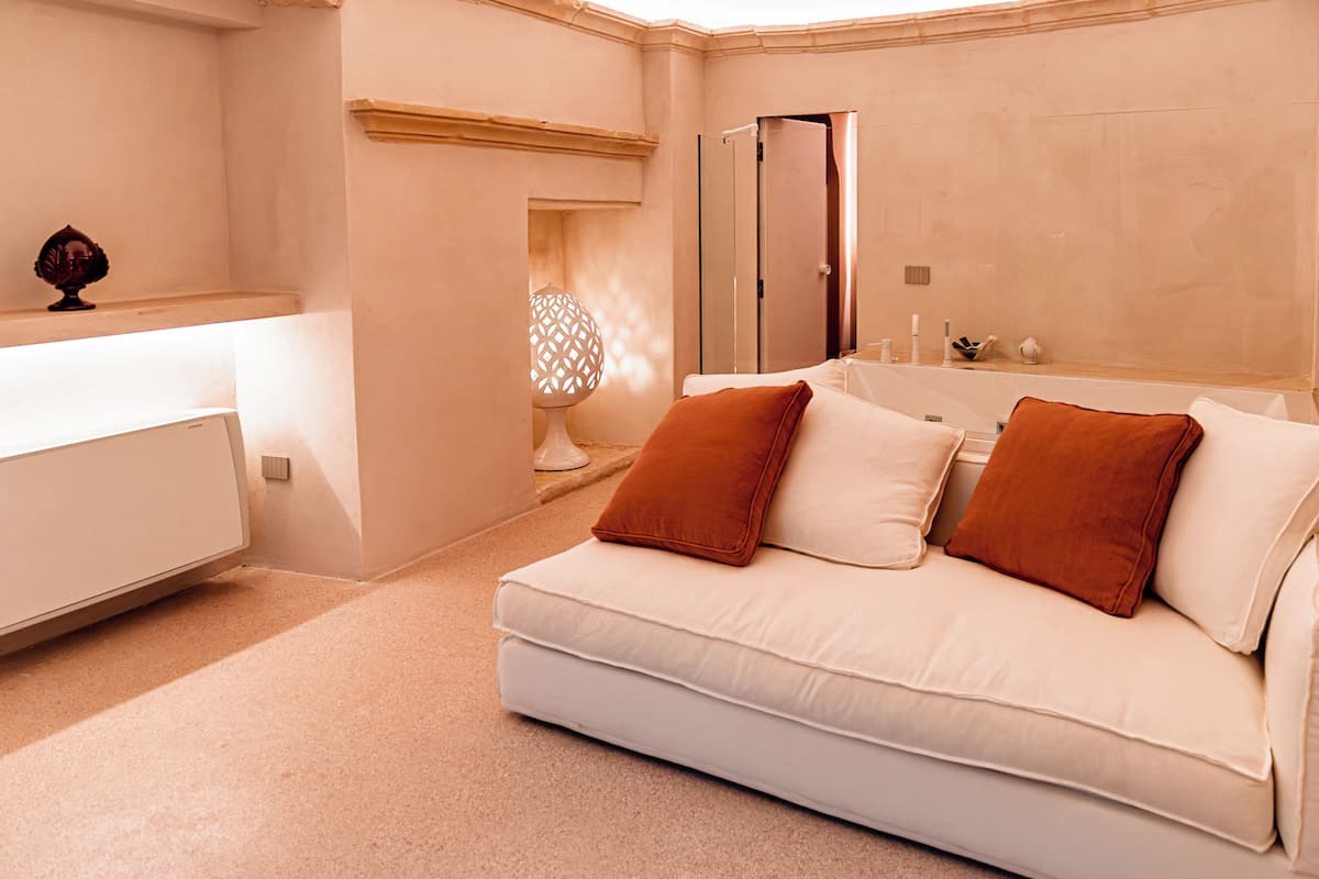 A modern bedroom with a white sofa, two brown pillows, a white bedside table, and a large mirror.