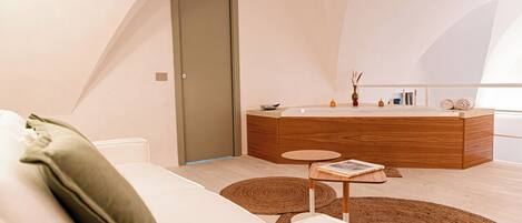 A modern bedroom with a white sofa, a wooden bedside table, a round rug, and a large window.