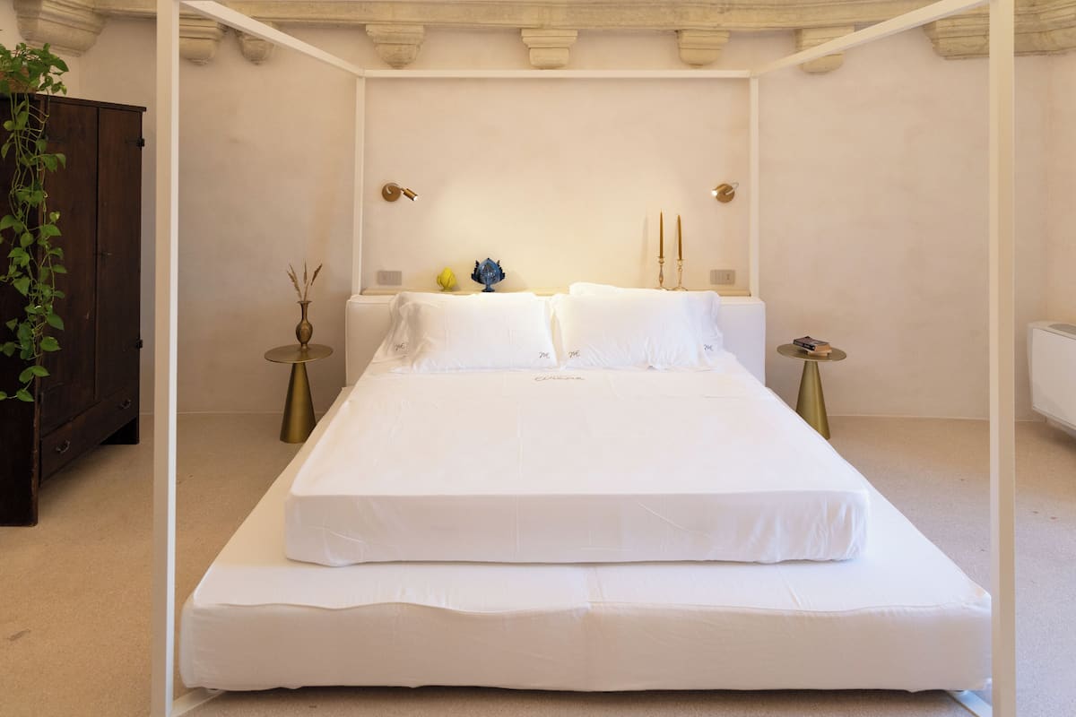 A bedroom with a large bed, two bedside tables, a nightstand, a potted plant, and a wooden wardrobe.