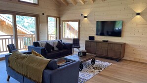 A spacious living room with a large sofa, a coffee table, and a TV mounted on the wall. - Magnificent Chalet - Swimming pool & exceptional view (Les Avanchers-Valmorel)