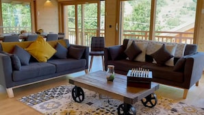 A cozy living room with two sofas, a coffee table, and a chessboard. Large windows offer a view of the outdoors. - Magnificent Chalet - Swimming pool & exceptional view (Les Avanchers-Valmorel)
