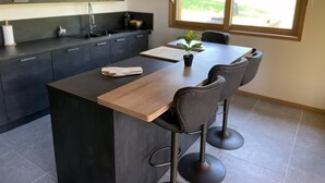 A modern kitchen with dark cabinets, a wooden island, and a dining area with a large window. - Magnificent Chalet - Swimming pool & exceptional view (Les Avanchers-Valmorel)