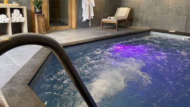 A modern indoor pool with a glass enclosure, a lounge chair, and a towel rack. - Magnificent Chalet - Swimming pool & exceptional view (Les Avanchers-Valmorel)