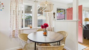 A dining area with a round table, wicker chairs, a hanging light fixture, and a window with curtains. - Garden Casita-Walk to Town (Arcata)