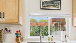 A kitchen with a stainless steel sink, wooden cabinets, a window with a view of a garden, and various kitchen utensils on the counter. - Garden Casita-Walk to Town (Arcata)