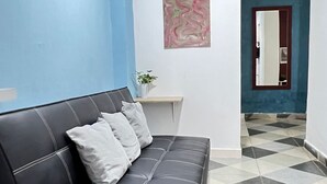 Un soggiorno moderno con un divano in pelle nera, un piccolo tavolino bianco con una pianta e un quadro astratto colorato appeso al muro.