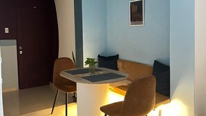Zona pranzo con un tavolo rotondo, due sedie, una pianta in vaso e un divano con cuscini.