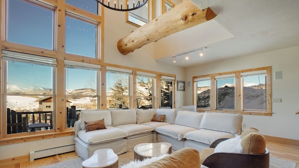 A spacious living room with a large sectional sofa, a coffee table, and a fireplace. Large windows offer views of a snowy landscape. - Walk to Lift! Luxe, Updated CBMR Home w/ Mtn Views (Gunnison)