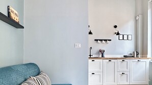 A modern living room with a teal sofa and a striped pillow, leading to a kitchen with white cabinets and a wooden countertop. - Colosseum Apartment 23 (Roma)