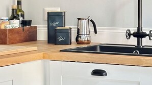 A modern kitchen with white cabinets, a black faucet, a coffee machine, and a black pendant light. - Colosseum Apartment 23 (Roma)