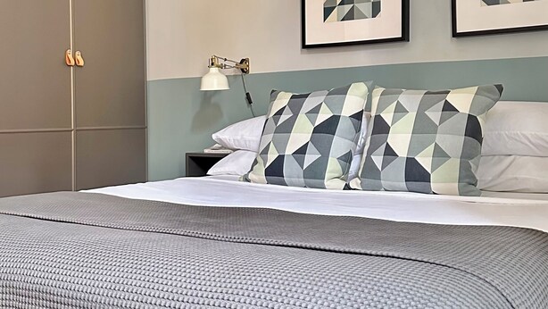 A neatly arranged bedroom with a bed, pillows, a nightstand, and two framed pictures on the wall. - Colosseum Apartment 23 (Roma)