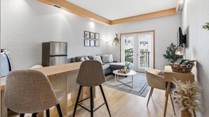 Un salon moderne avec un canapé, un coin repas avec des chaises, une cuisine équipée d’un réfrigérateur et un balcon avec vue.