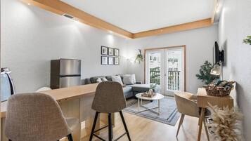 Ein modernes Wohnzimmer mit einer Couch, einem Essbereich mit Stühlen, einer Küche inklusive Kühlschrank und einem Balkon mit Blick.