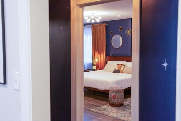 Quarto com cama, mesa de cabeceira, luminária e um espelho decorativo na parede.
